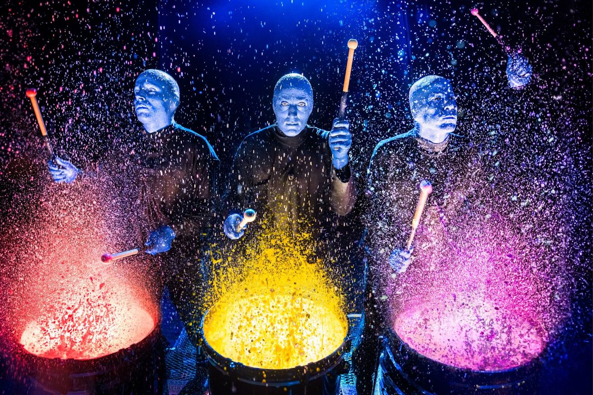 The Blue Man Group drumming on paint-covered drums.