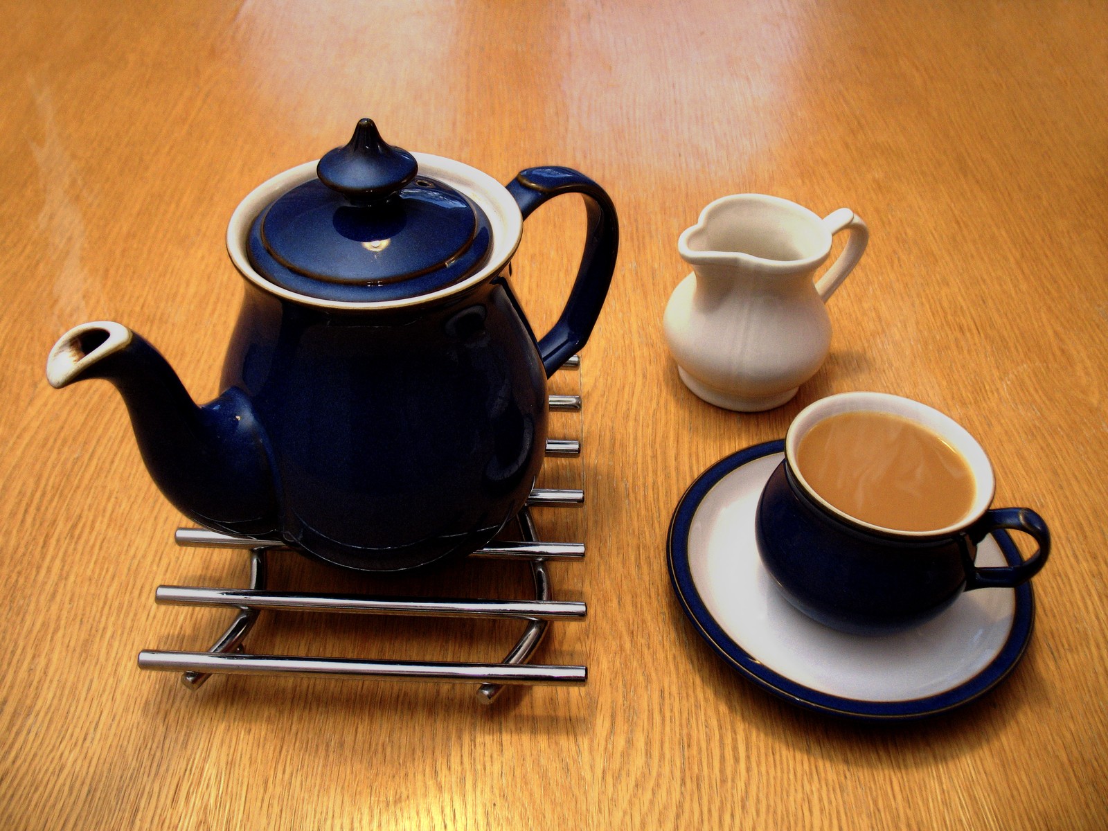 A teapot, a milk jug, and a cup of tea with milk.